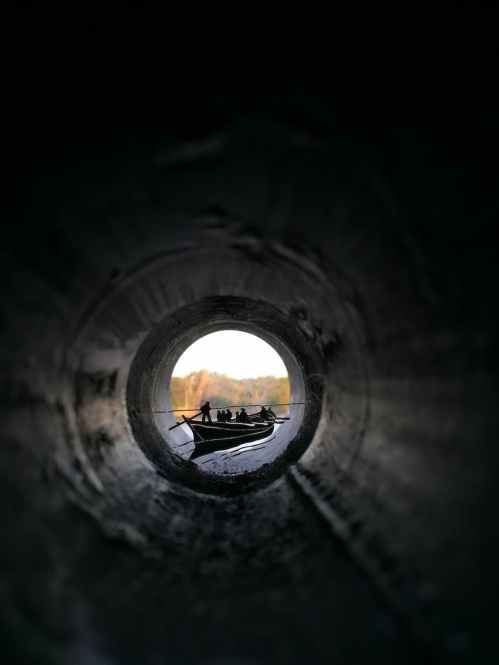 people riding canoe boat view from inside pipe